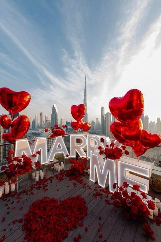 LED Letters ‘MARRY ME’ Marquee with Red Heart-Shaped Foil Balloons, Artificial Red Petals, Red Flowers Arrangement and White Candles on Small Glass Cylinder - Proposal Perfect for special occasions