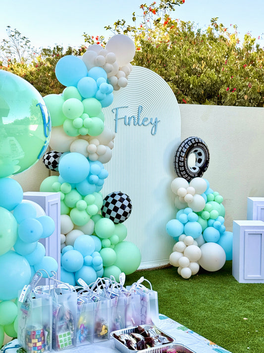 Chiara Wall with Customizable Name, 3 White Cake Stand with Balloons Car-Themed Decor Blue, Mint Green, Sand White with Wheels and Checkered Foil Balloons Accents  - Perfect for special occasions