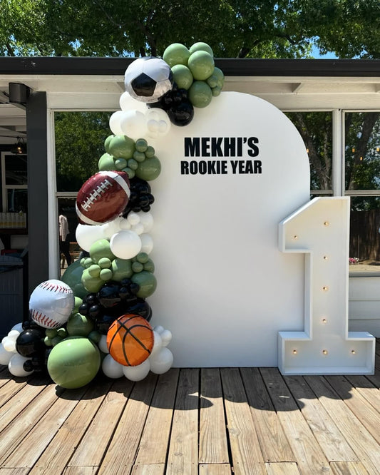 Customizable Board Backdrop with Balloon Green, Black and White with Sports Ball Balloon Accents and LED Marquee Number ‘1’ - Sports-Themed Perfect for special occasions