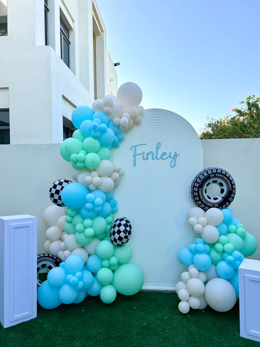 Chiara Wall with Customizable Name, 3 White Cake Stand with Balloons Car-Themed Decor Blue, Mint Green, Sand White with Wheels and Checkered Foil Balloons Accents  - Perfect for special occasions