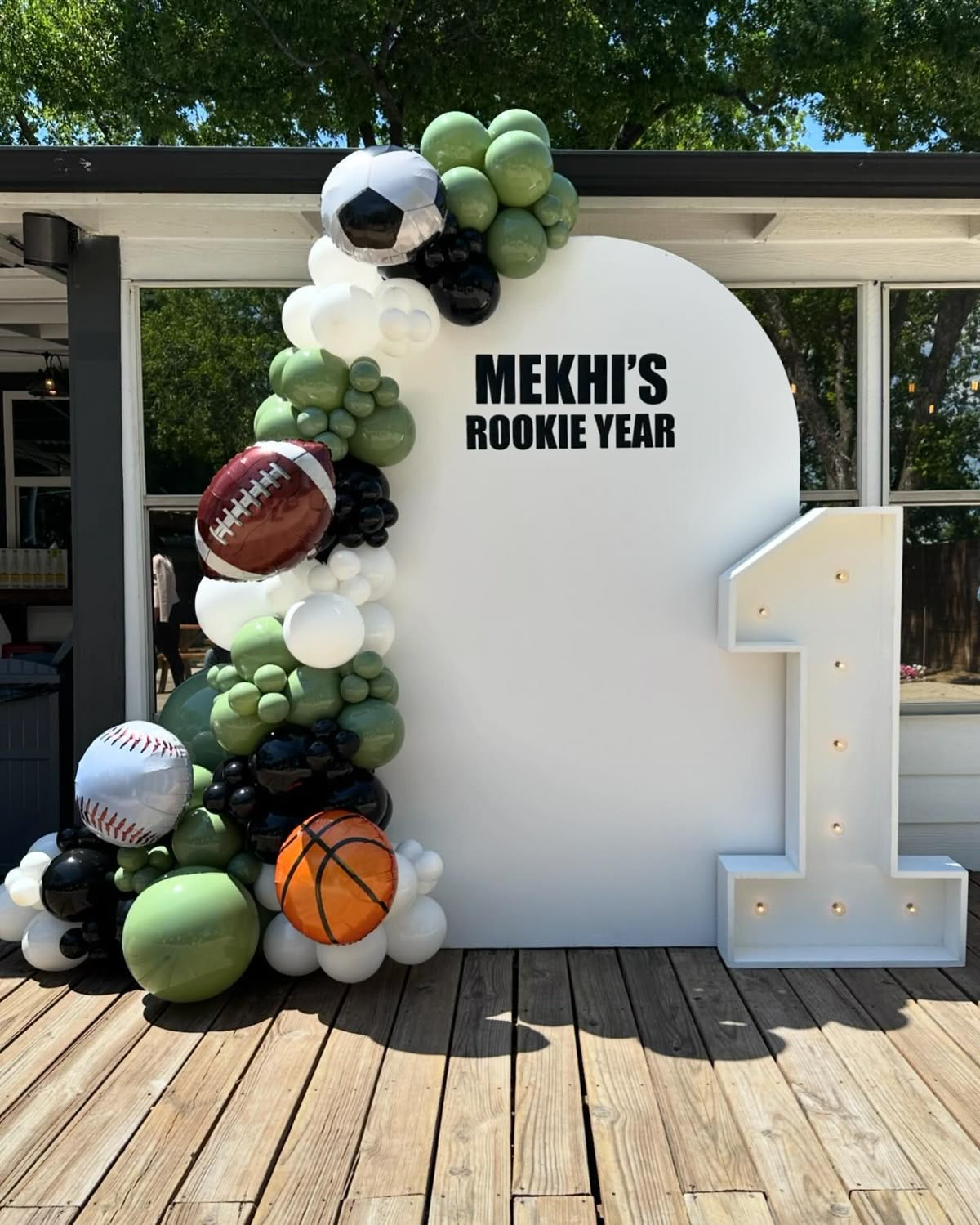 Customizable Board Backdrop with Balloon Green, Black and White with Sports Ball Balloon Accents and LED Marquee Number ‘1’ - Sports-Themed Perfect for special occasions