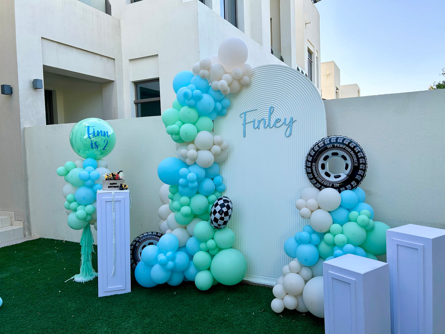 Chiara Wall with Customizable Name, 3 White Cake Stand with Balloons Car-Themed Decor Blue, Mint Green, Sand White with Wheels and Checkered Foil Balloons Accents  - Perfect for special occasions
